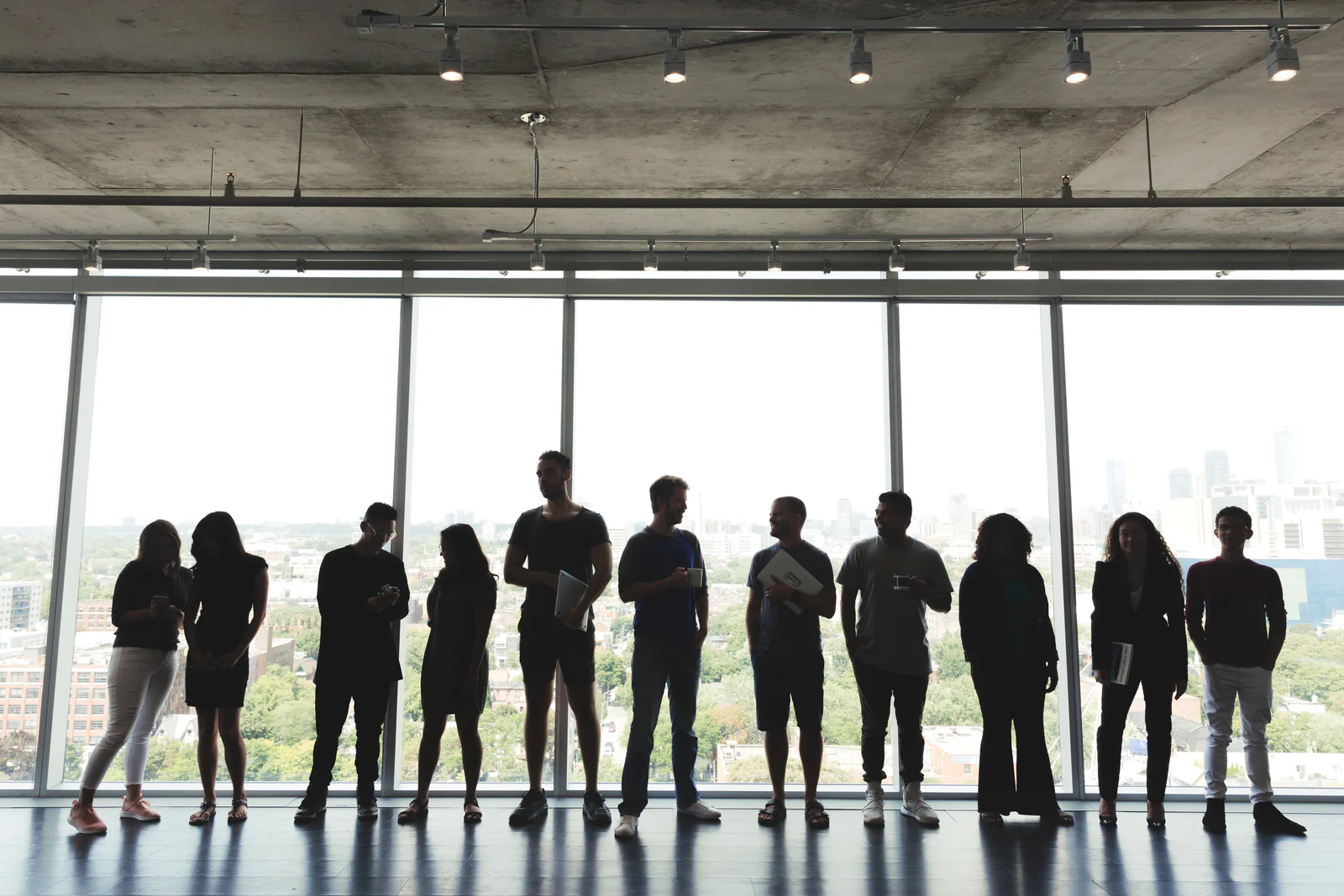 Diverse group of individuals silhouetted against a large modern window