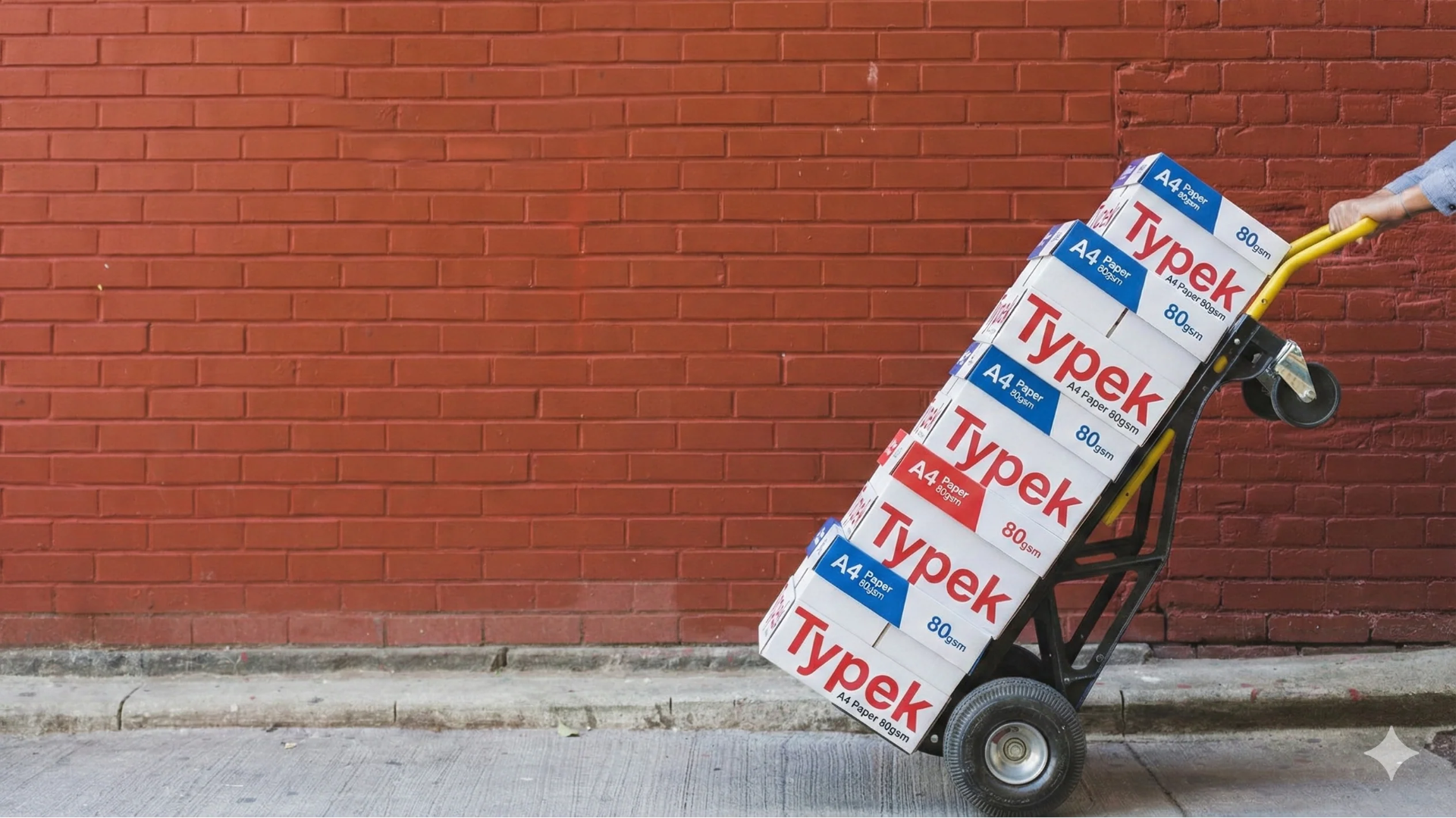 Hand truck transporting stacked boxes of Typek paper against a brick wall
